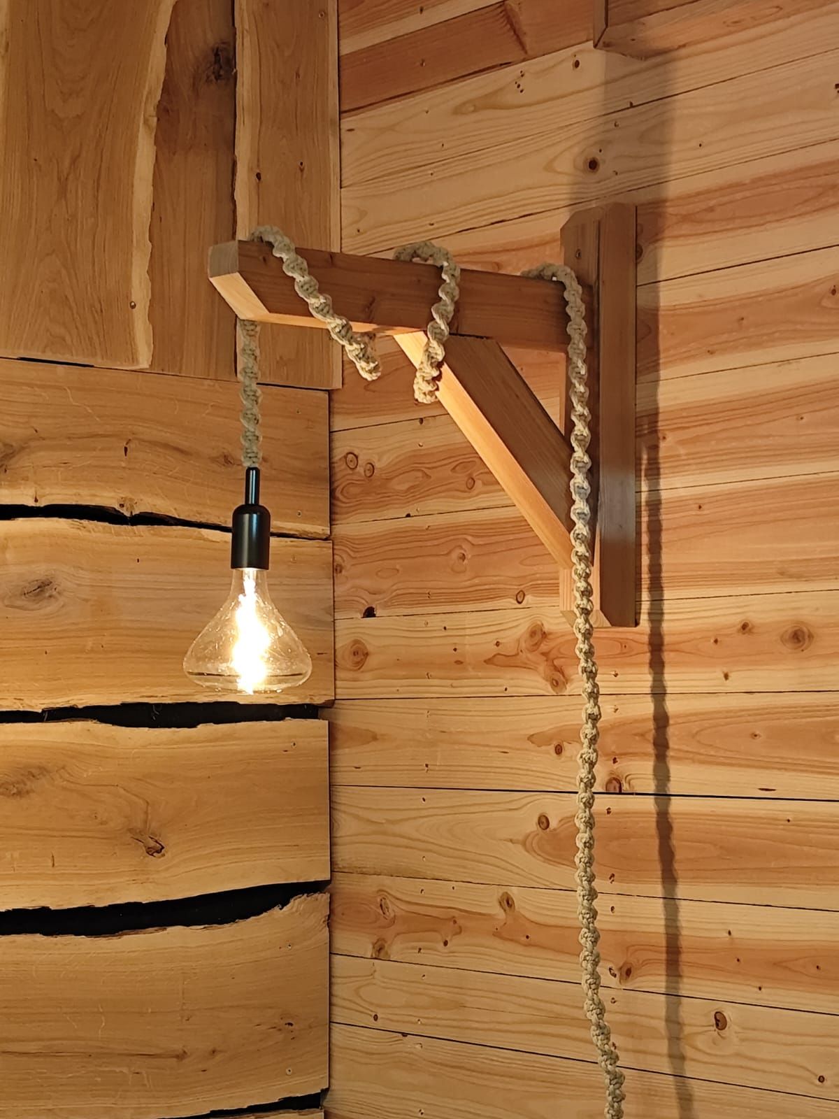 Une ampoule nue suspendue à un fil électrique à côté d'une petite étagère en bois sur un mur rustique.
