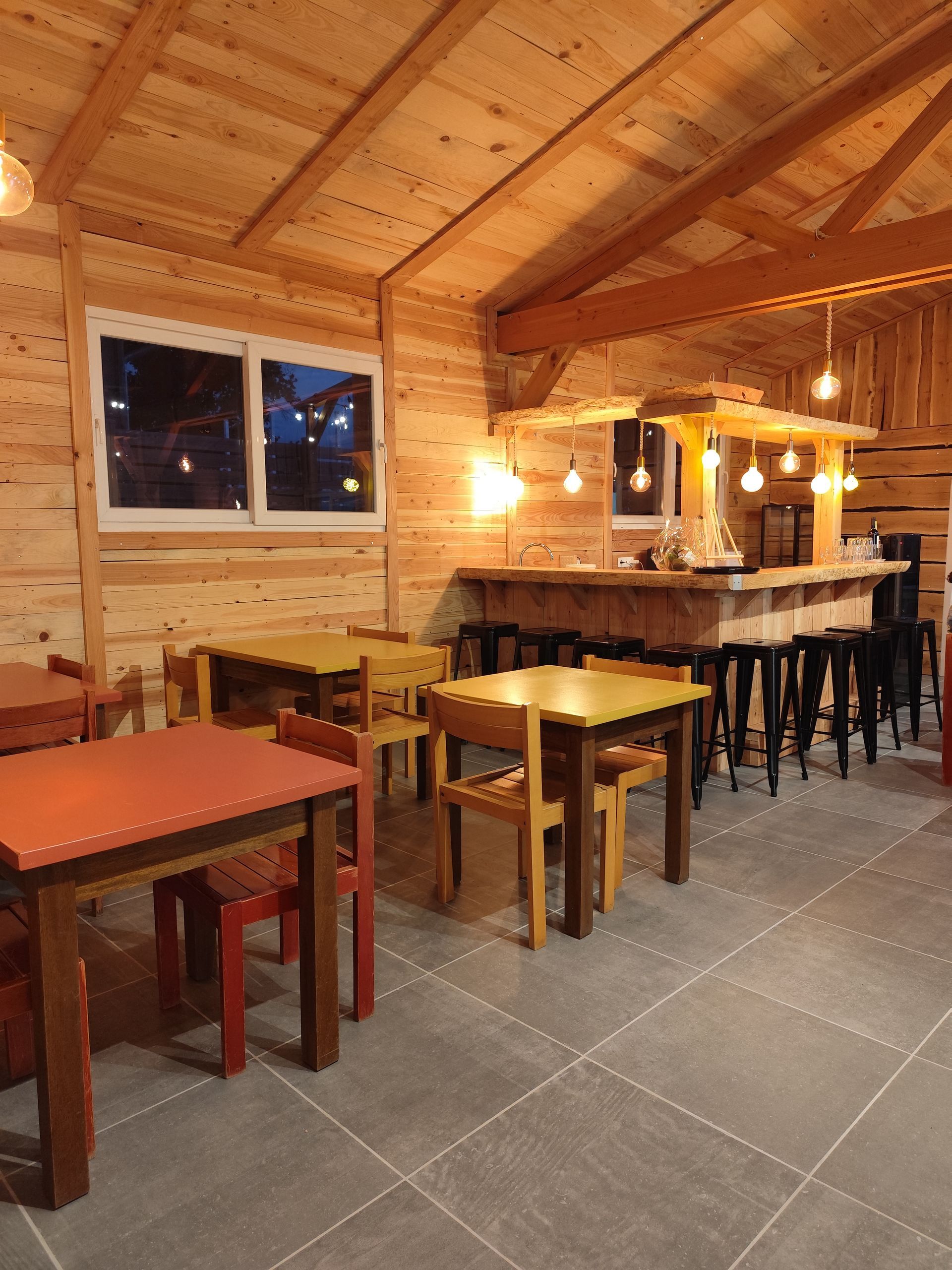 Restaurant chaleureux de style chalet en bois avec tables vides, tabourets de bar, éclairage tamisé et un mur vitré