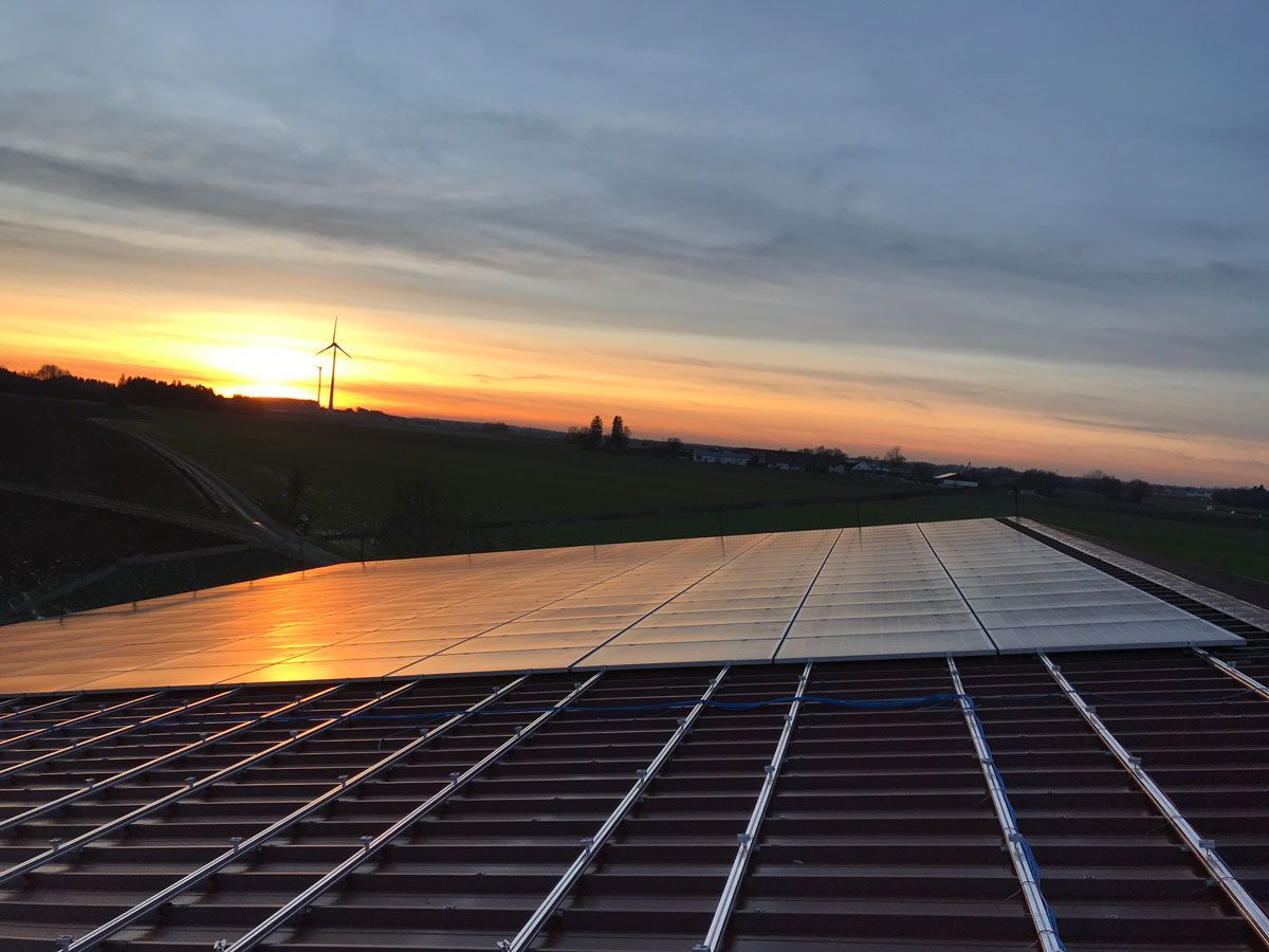 Sonnenuntergang über einem Dach mit einer Windkraftanlage im Hintergrund