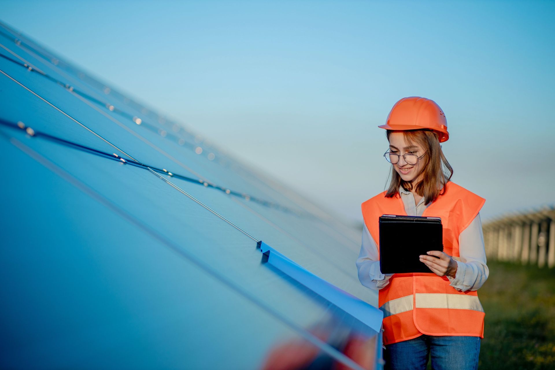 Una mujer con casco sostiene una tableta frente a un panel solar.