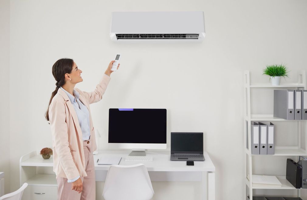 Una mujer está usando un control remoto para encender un aire acondicionado en una oficina.