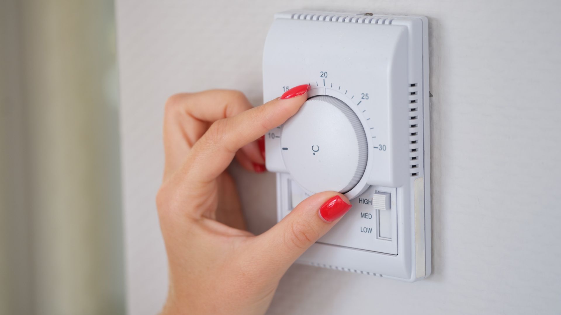 Una mujer está ajustando un termostato en una pared.