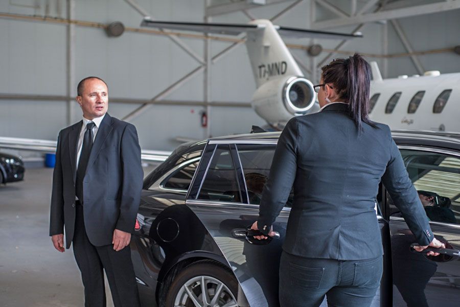 A man and a woman are standing next to a car in a hangar.