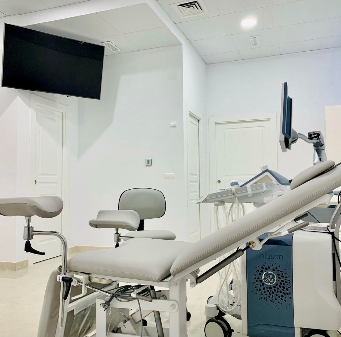 Sala de reconocimiento médico con sillón de reconocimiento y ecógrafo. Paredes blancas.