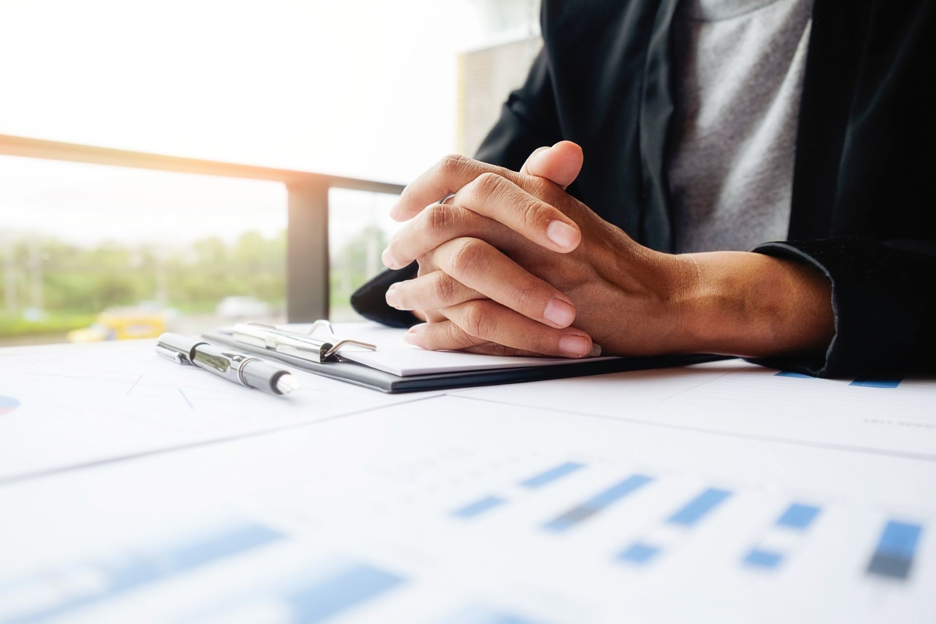 Manos unidas sobre un escritorio con un portapapeles y gráficos, probablemente en una oficina