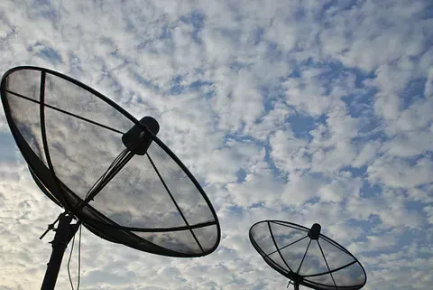 Dos antenas parabólicas contra un cielo azul con nubes blancas esponjosas.