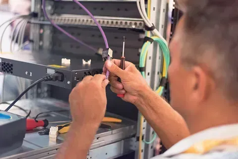 Un hombre repara cables de red en un rack de servidores utilizando un destornillador.