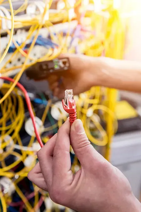 Mano sosteniendo un cable Ethernet rojo cerca de un rack de servidores enredado.