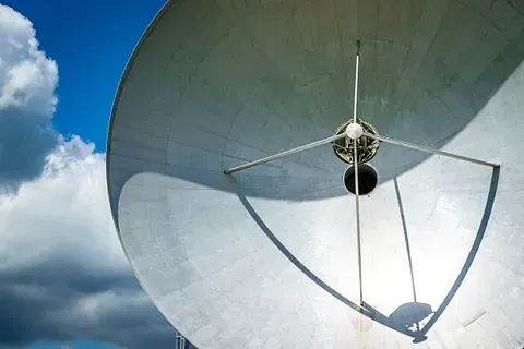 Antena parabólica de gran tamaño contra un cielo azul con nubes.
