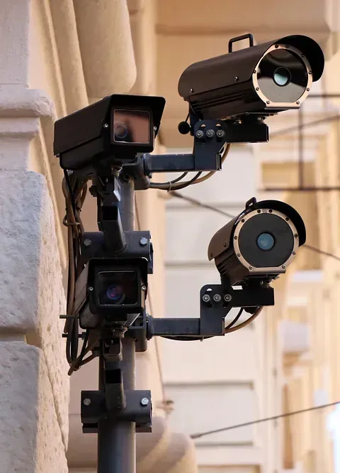 Tres cámaras de seguridad negras montadas en un poste, orientadas hacia un edificio.