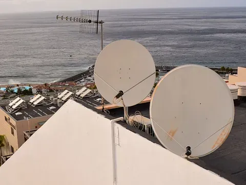 Dos antenas parabólicas en una azotea con vistas al océano y a los edificios.