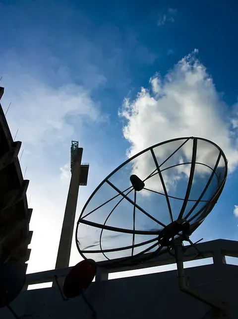 Silueta de una gran antena parabólica contra un cielo azul brillante con nubes, montada en un tejado.