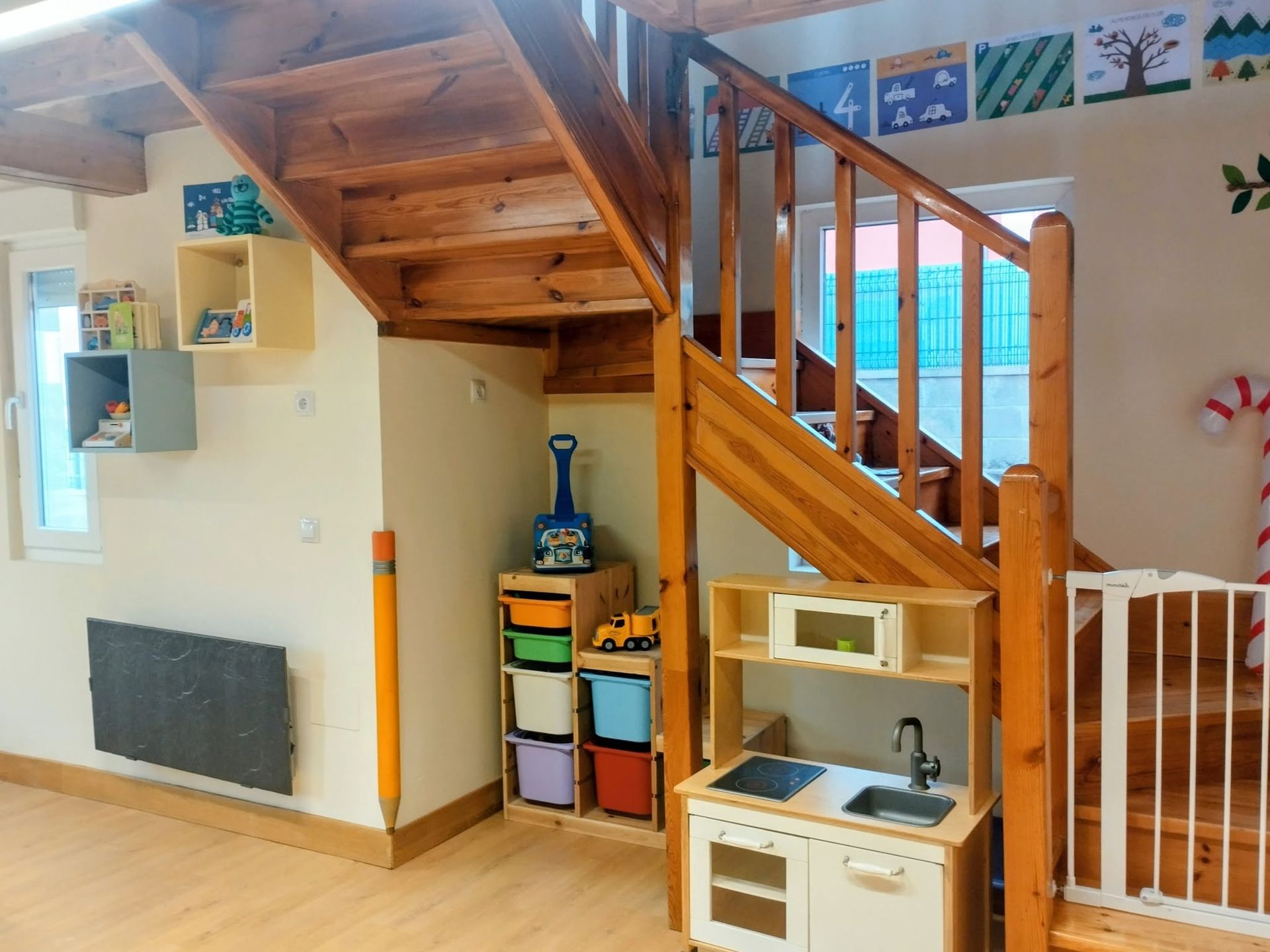 Zona de juegos infantiles con escaleras de madera, casitas coloridas y una cocinita de juguete bajo el altillo.