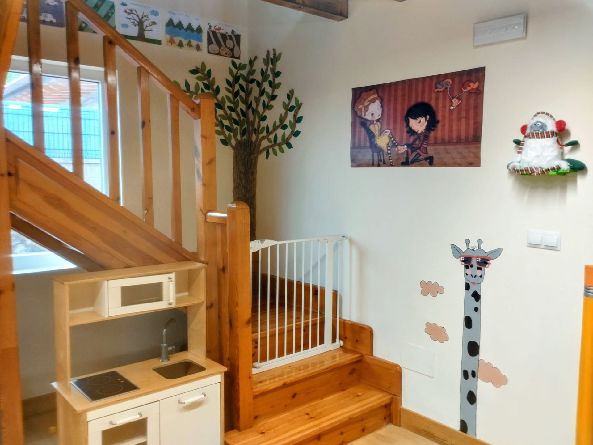 Entrada con escaleras de madera, puerta de seguridad para niños, escritorio, decoración de pared y vinilo de jirafa.