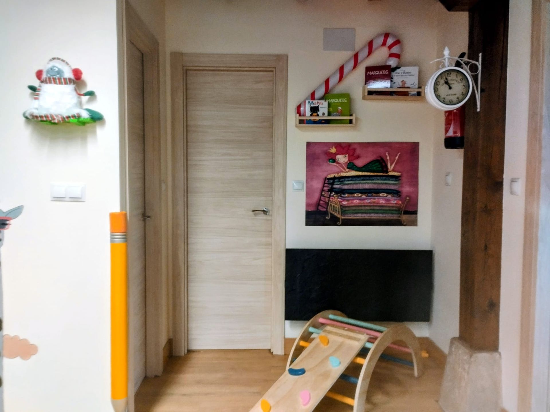 Pasillo interior colorido con un televisor montado en la pared, estantes, una puerta cerrada y una tienda de juegos