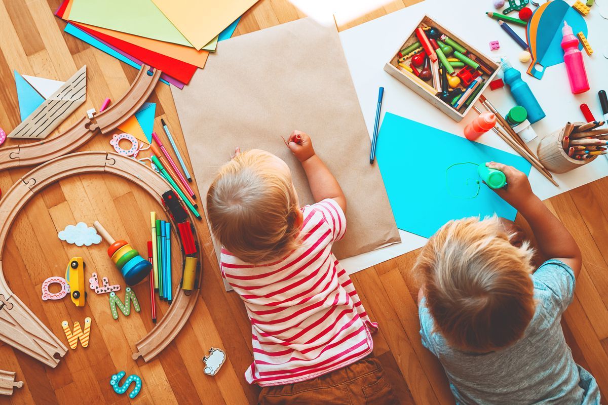 Dos niños haciendo coloridas manualidades de papel en una mesa de madera con materiales esparcidos.