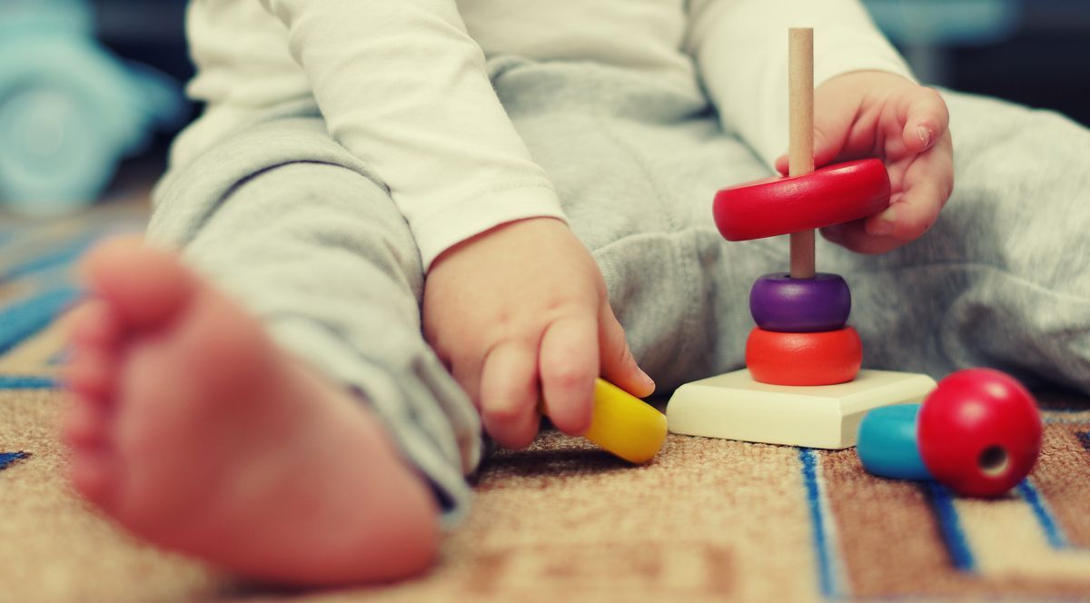Bebé jugando con coloridos juguetes de madera apilables en el suelo.
