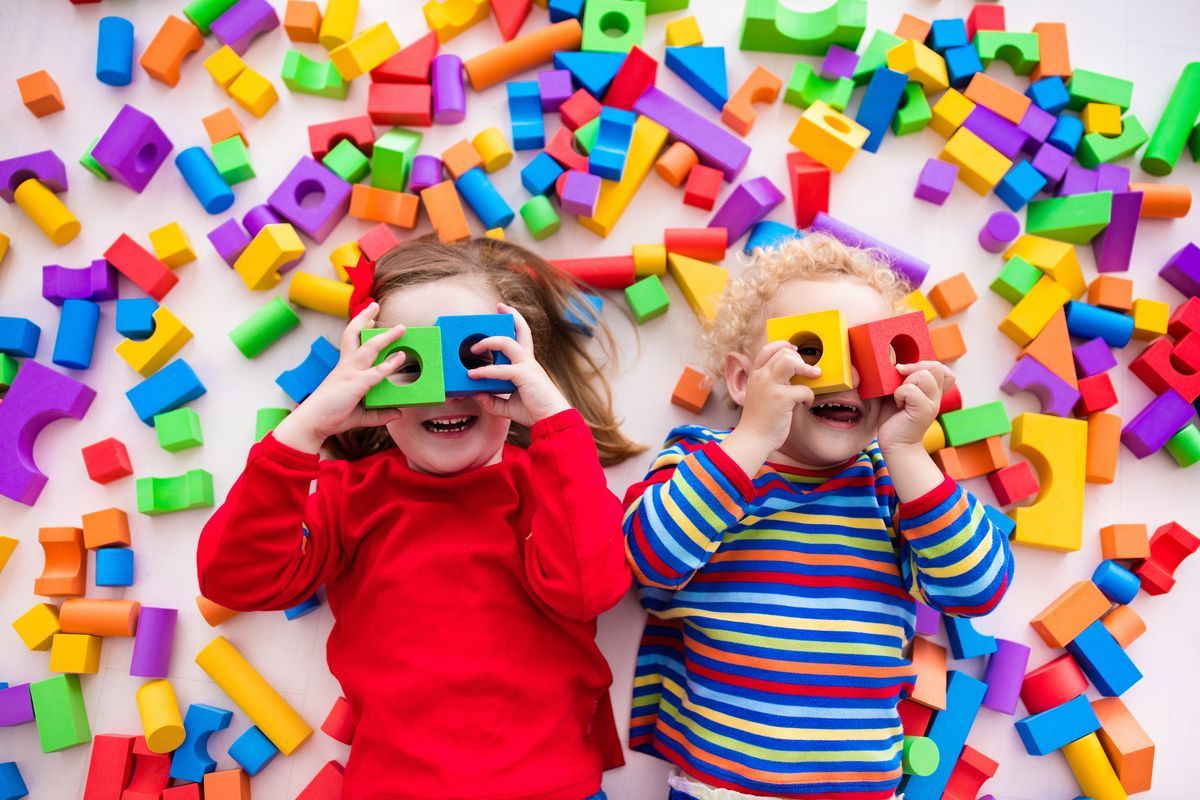 Dos niños sobre bloques de colores sostienen cámaras de juguete entre bloques de plástico brillantes dispersos.
