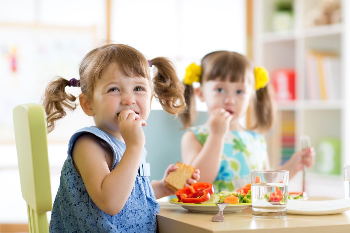 Dos niños comiendo bocadillos en una mesa de cocina luminosa.