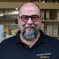 Zwei Personen in schwarzen Poloshirts stehen draußen. Die Frau lächelt, der Mann hat einen Bart.