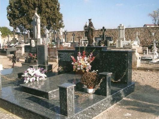 Escena de cementerio con varias lápidas de granito y marcadores de tumbas, algunos con arreglos florales.