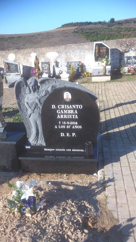 Lápida de granito negro en un cementerio; ángel tallado a la izquierda, nombre y fechas inscritos.