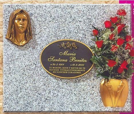 Lápida con rostro de bronce, placa y rosas. Fondo de granito gris.