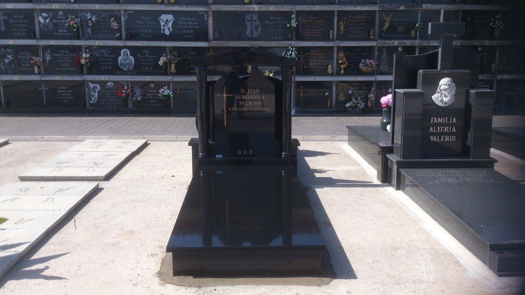 Lápidas de granito negro en un cementerio, con una estructura central y múltiples nichos al fondo.
