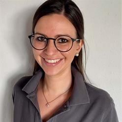 Eine Frau mit Brille und Halskette lächelt in die Kamera.