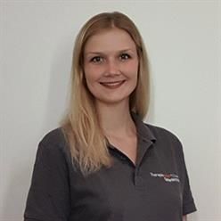 Eine Frau in einem grauen Hemd lächelt in die Kamera.