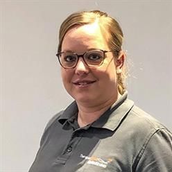 Eine Frau mit Brille und grauem Hemd lächelt in die Kamera.