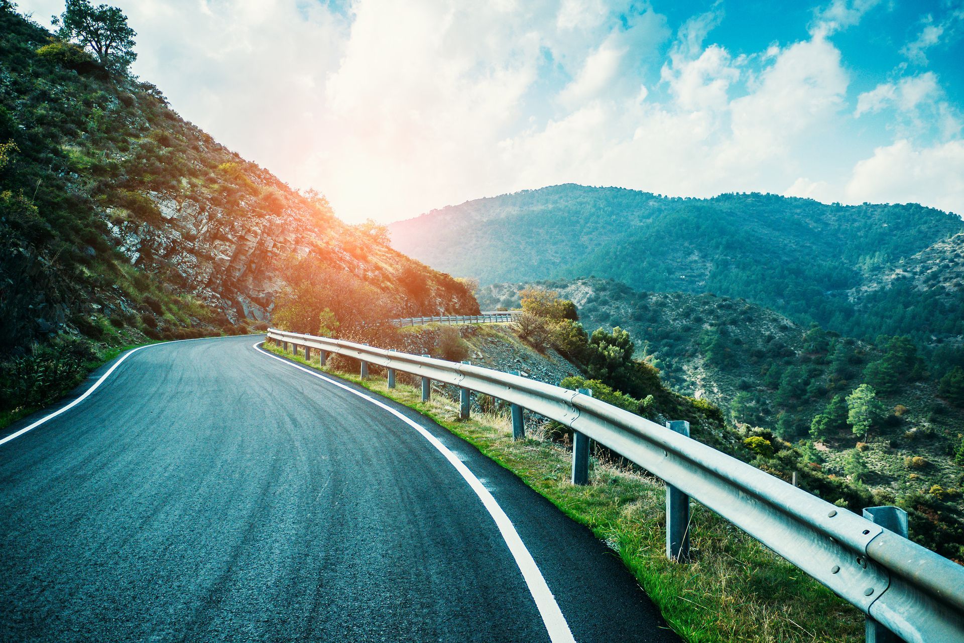 Un camino que atraviesa una zona montañosa con el sol brillando a través de los árboles.