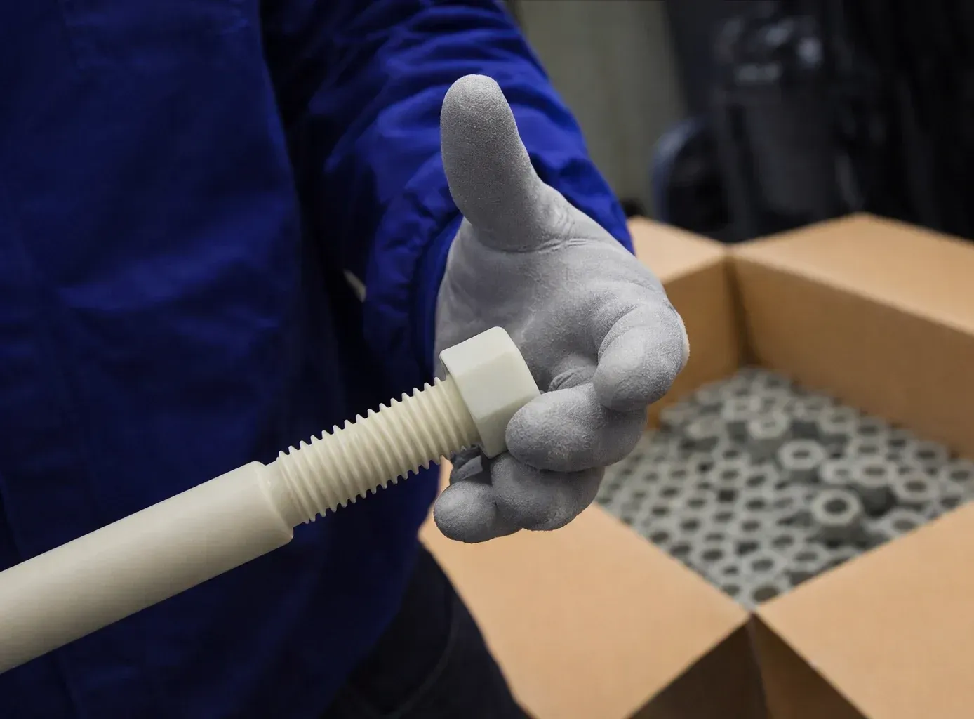 Un trabajador que usa gafas de seguridad y guantes manipula tubos de plástico gris junto a una máquina de moldeo