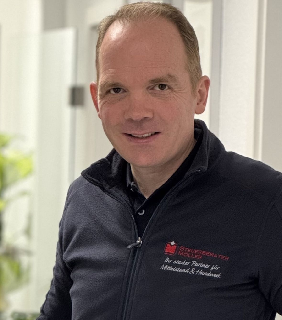 Ein Mann mit Glatze und weißem Hemd lächelt in die Kamera.