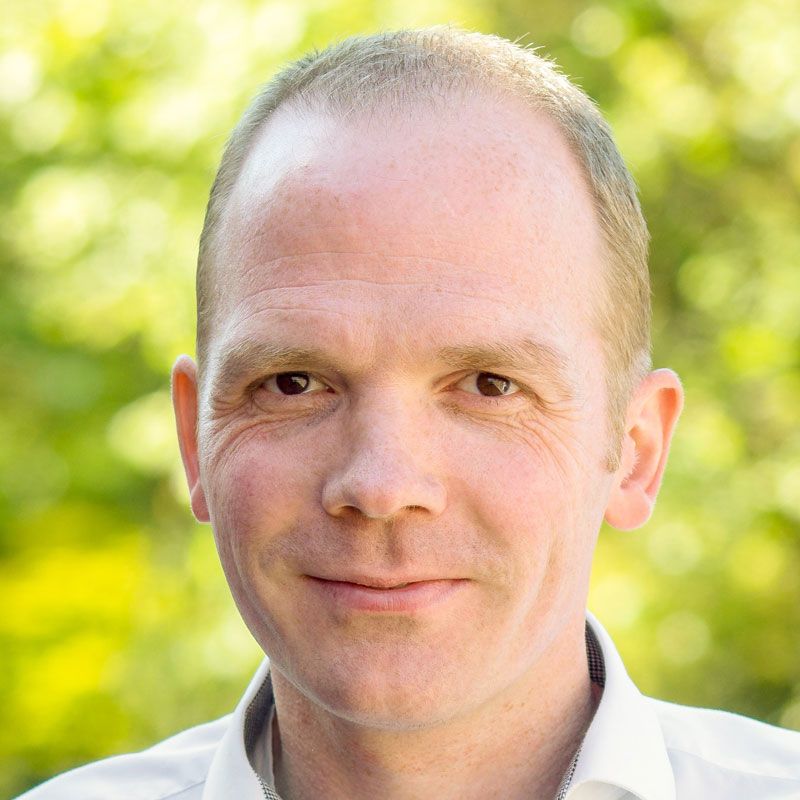 Ein Mann im weißen Hemd lächelt in die Kamera.