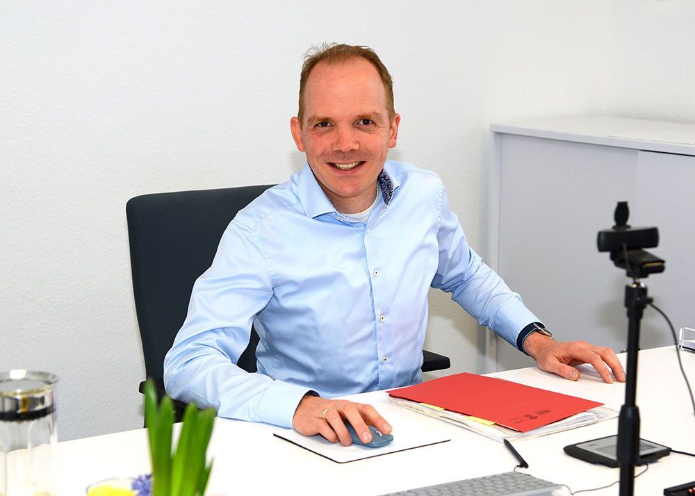 Ein Mann in einem blauen Hemd sitzt an einem Schreibtisch und benutzt eine Computermaus.