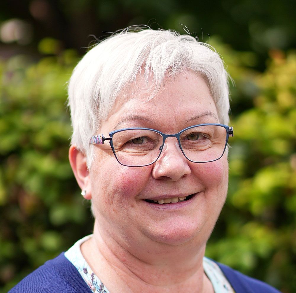 Eine Frau mit Brille und blauem Pullover lächelt in die Kamera.