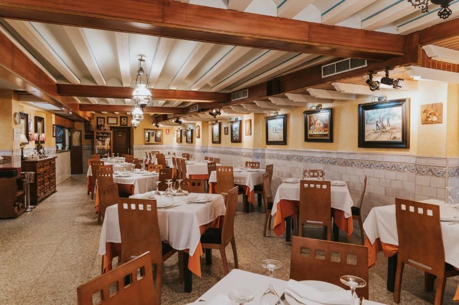 Comedor rústico de restaurante con vigas de madera, manteles blancos y obras de arte enmarcadas en las paredes.
