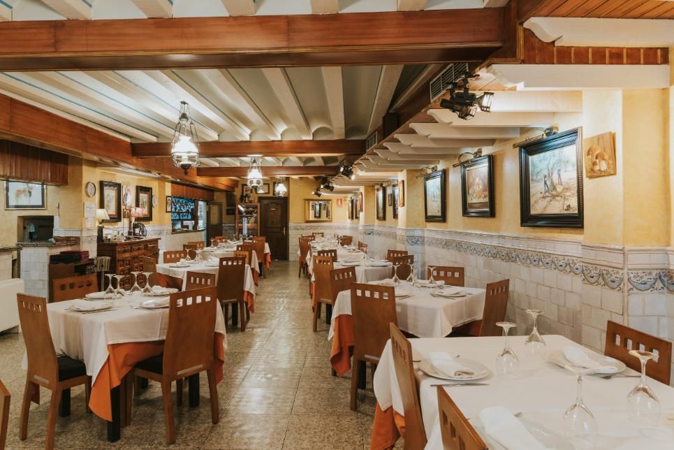 Comedor vacío de un restaurante con manteles blancos, sillas de madera y una cálida decoración rústica.