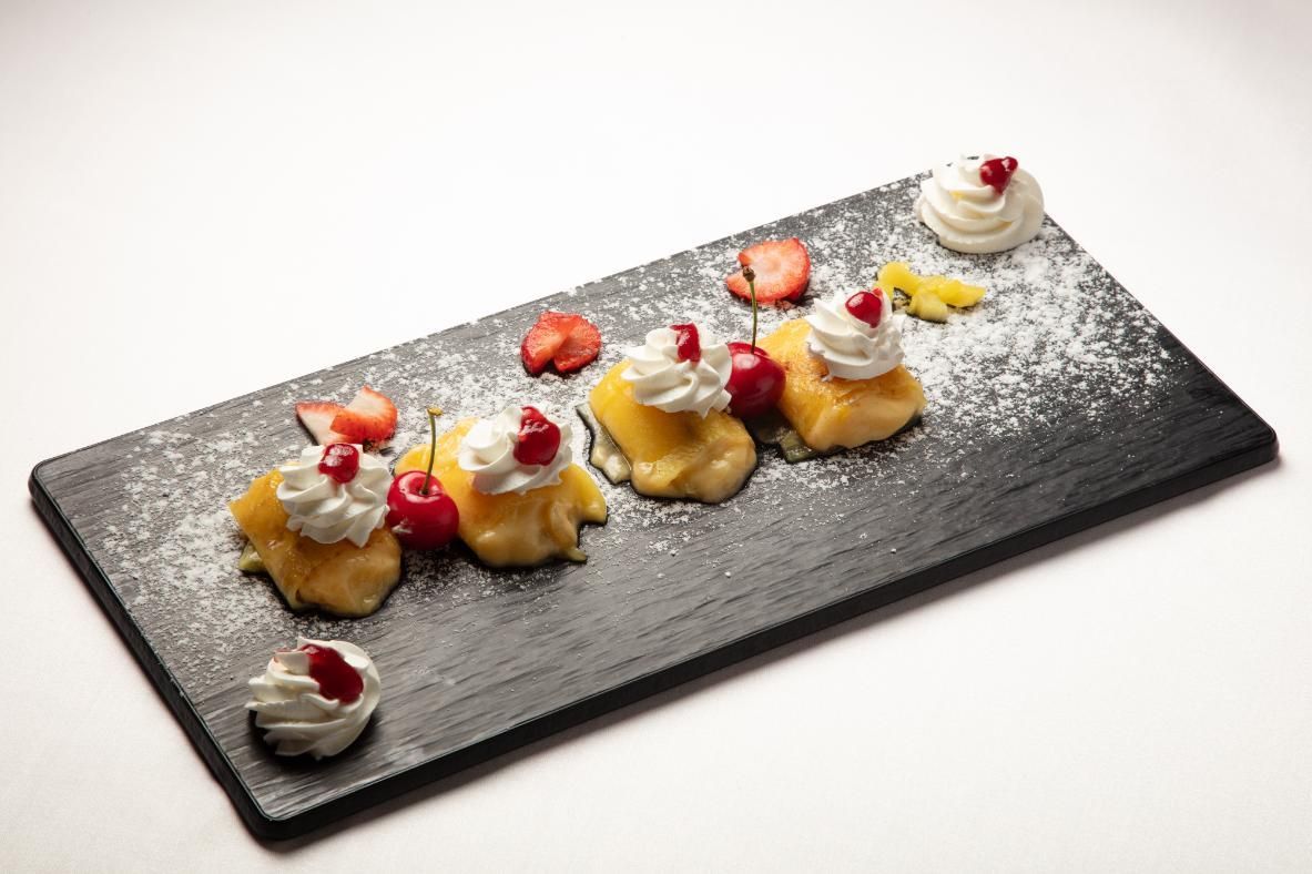 Plato de postre con pasteles decorados con frutas sobre una pizarra negra, espolvoreado con azúcar glas.