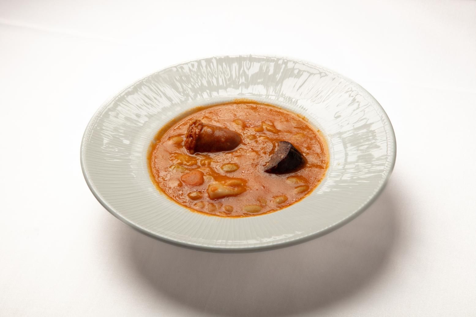 Un tazón de sopa cremosa de naranja con camarones y una guarnición oscura en un plato blanco.