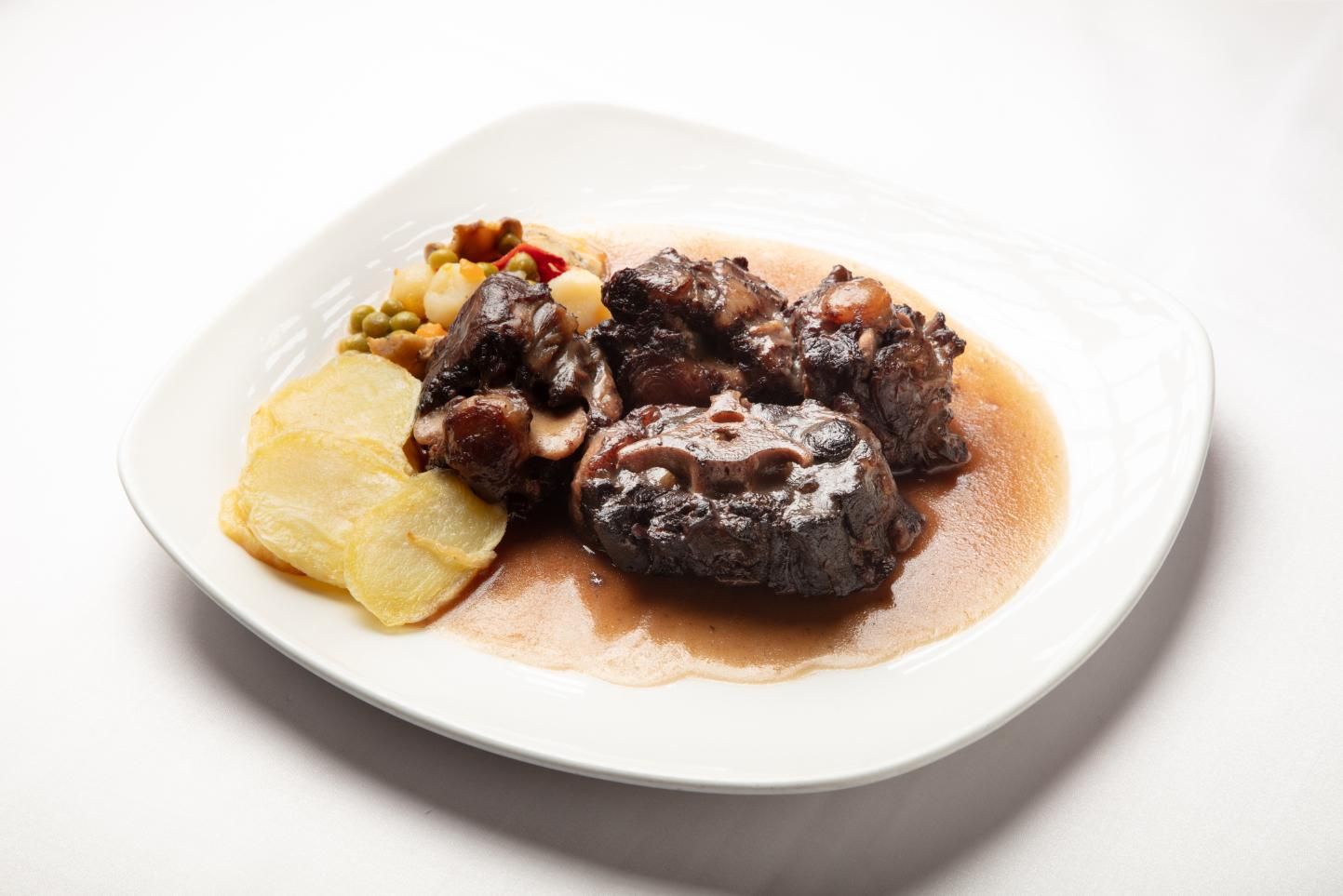 Carne estofada con salsa y patatas en un plato blanco.