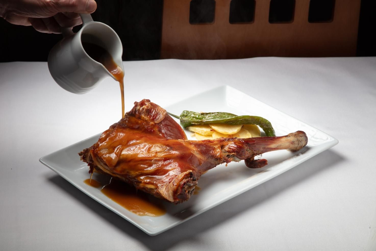 Muslo de pavo asado en un plato blanco con salsa y verduras encurtidas al lado.