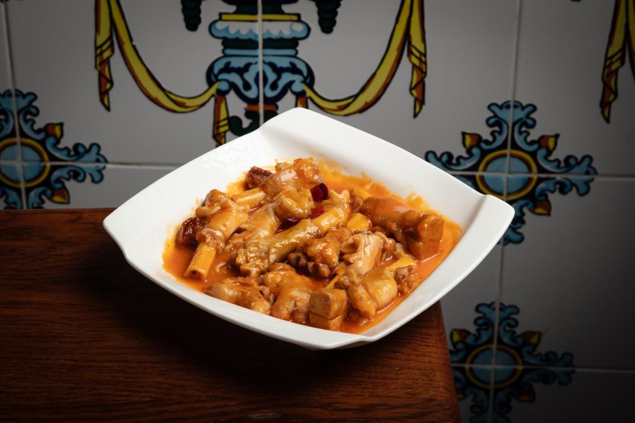 Un tazón blanco con pasta en salsa sobre una mesa de madera, con azulejos azules estampados al fondo.