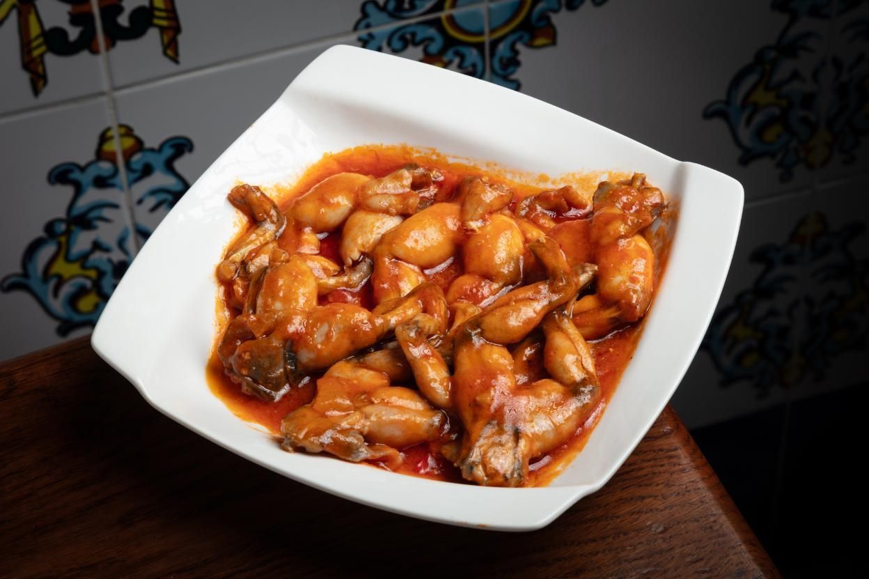 Un tazón blanco con alitas de pollo de color naranja brillante sobre una mesa.