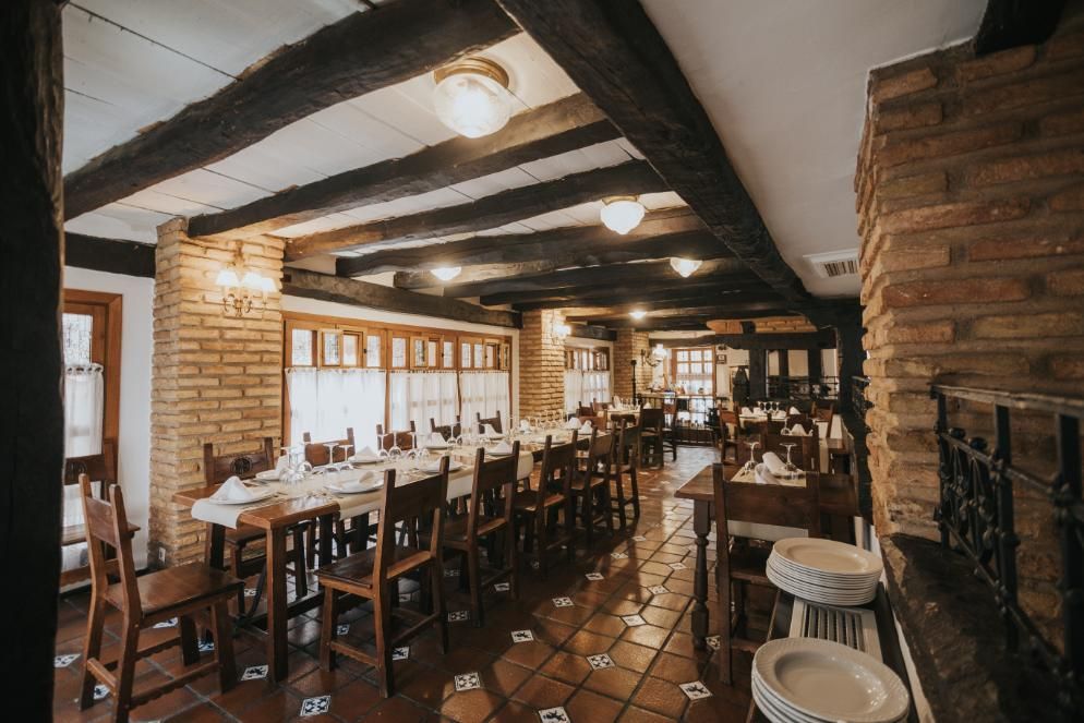 Interior acogedor y rústico del restaurante con mesas de madera, paredes de ladrillo y luces cálidas en el techo.