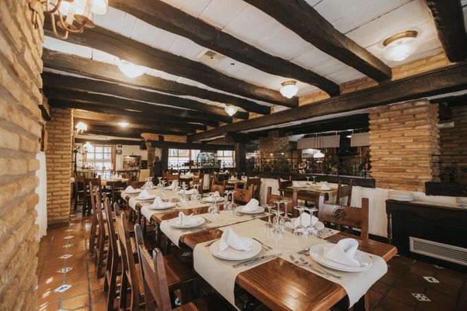 Elegante comedor de restaurante con mesas puestas, pilares de ladrillo visto y vigas de madera oscura.