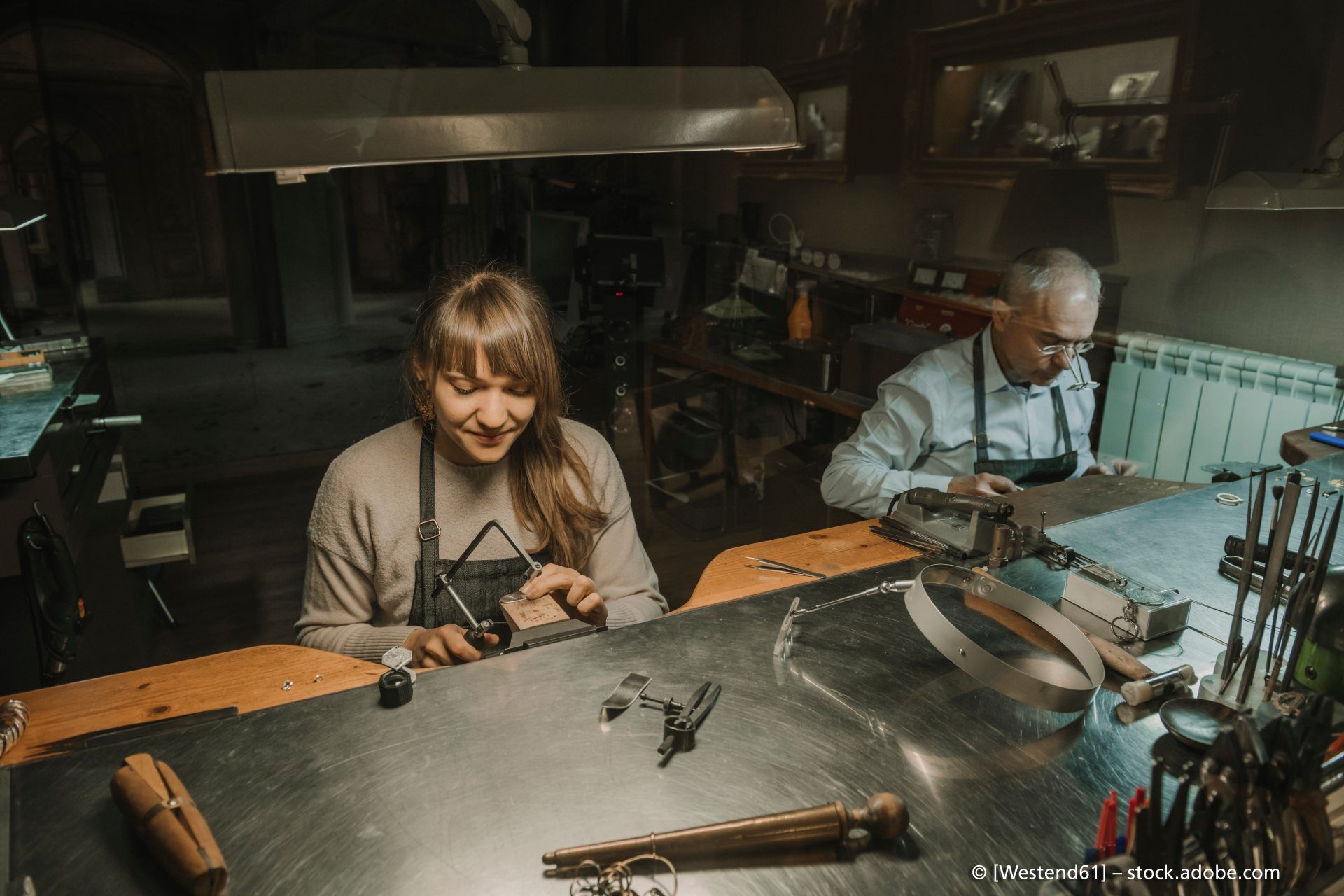 Goldschmiede Norys - ein Mann und eine Frau sitzen bei gedimmtem Licht an einer modernen Werkbank