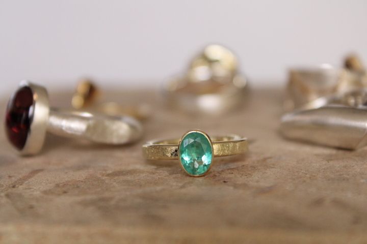 Handgefertigter Goldring mit ovalem Smaragd auf rustikalem Hintergrund – Schmuckdesign Goldschmiede Norys
