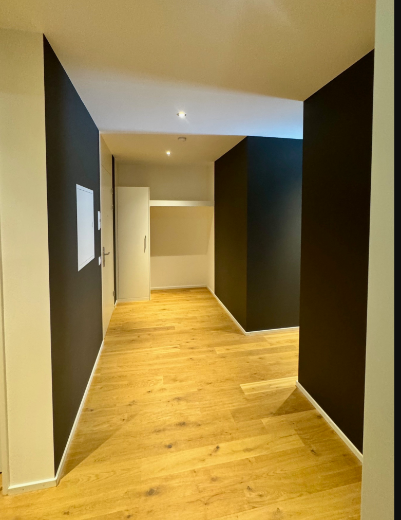 Zimmer mit abstraktem Wandbild, zwei Stühlen, kleinem Tisch und einer Tür. Farben: Blau, Orange und Weiss.